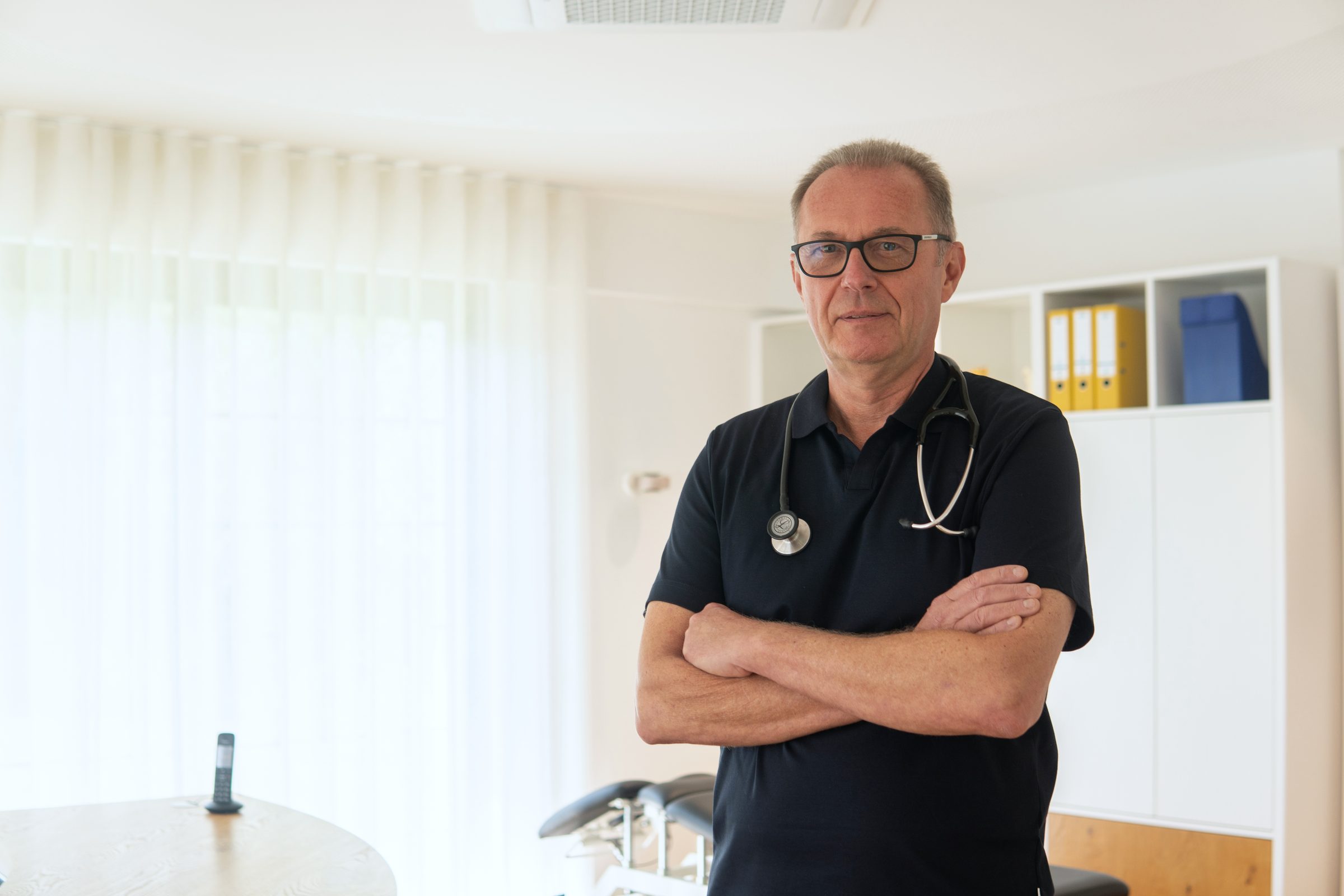 Dr. Stefan Balzer mit verschränkten Armen in seinem hellen Sprechzimmer